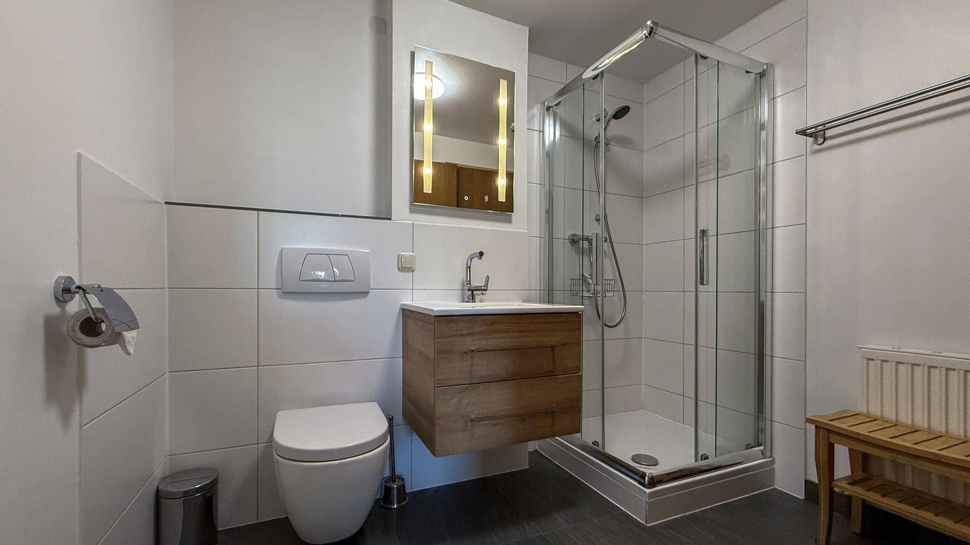 Zeitgemäßes Badezimmer mit Duschkabine, Waschtisch und WC, in hellen Farbtönen gehalten.