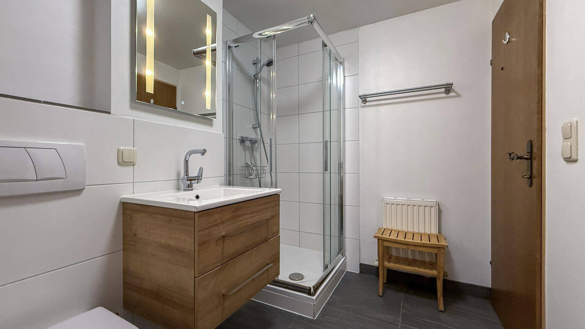 Modernes Badezimmer mit Duschkabine, schwebendem Waschtisch und Wand-WC, hell gefliest.