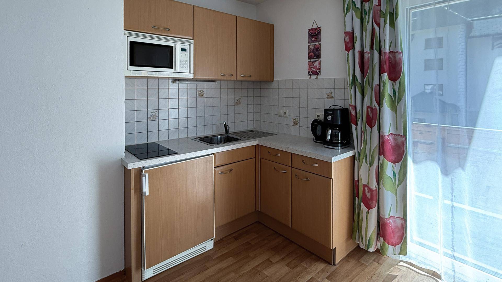 Kompakte Küchenzeile mit Kochfeld, Spüle, Mikrowelle und Kühlschrank, ideal für kleine Wohnungen.