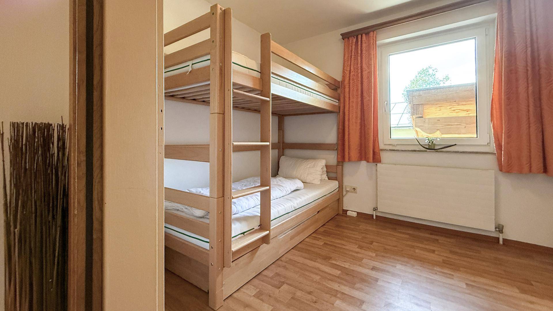 Helles Schlafzimmer mit Etagenbett und Fenster, das viel Tageslicht hereinlässt.