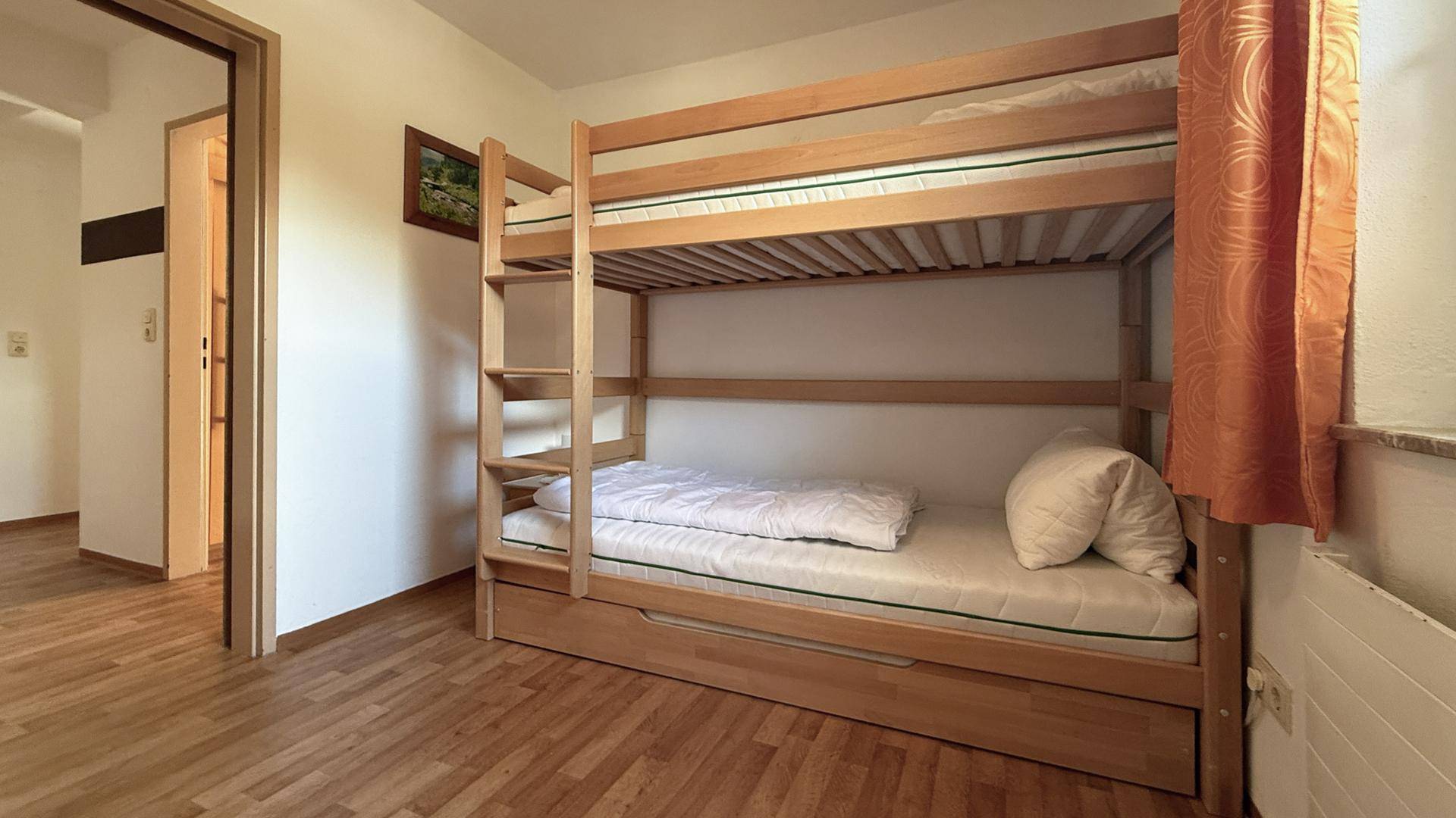 Kinderzimmer mit Etagenbett aus Holz und orangefarbenen Vorhängen, bietet Platz für mehrere Personen.