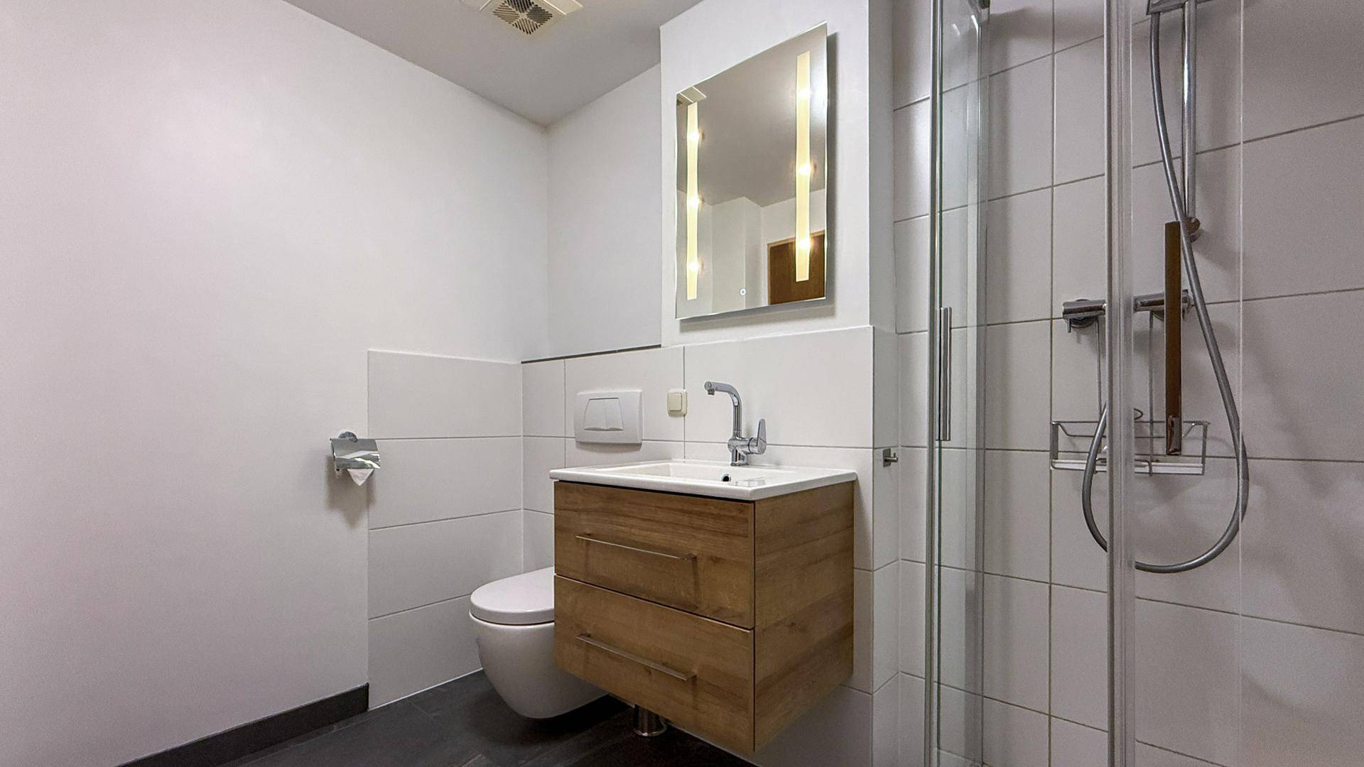 Helles Badezimmer mit modernem Waschtisch, Duschkabine und WC, ausgestattet mit Spiegel.