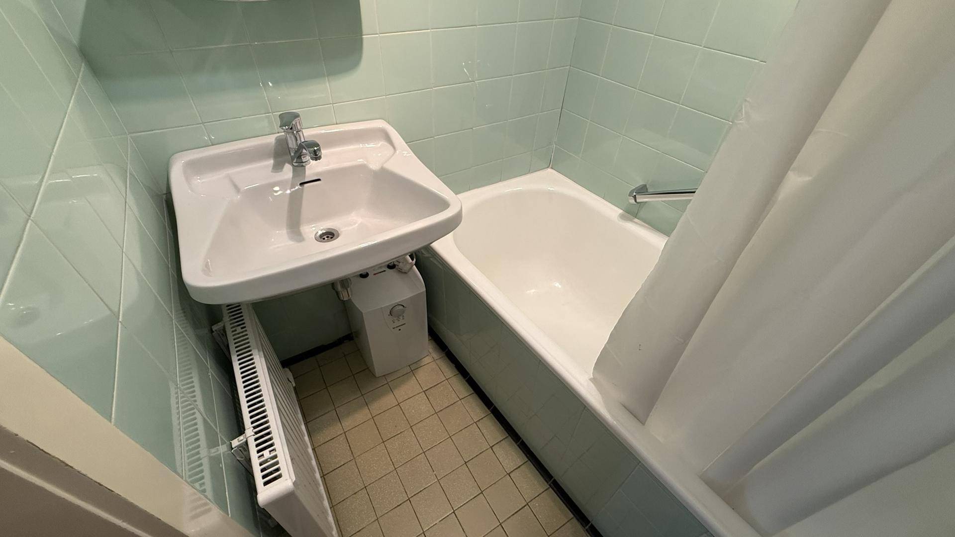Badezimmer mit Badewanne, Waschbecken und hellgrünen Fliesen an Wänden und Boden.