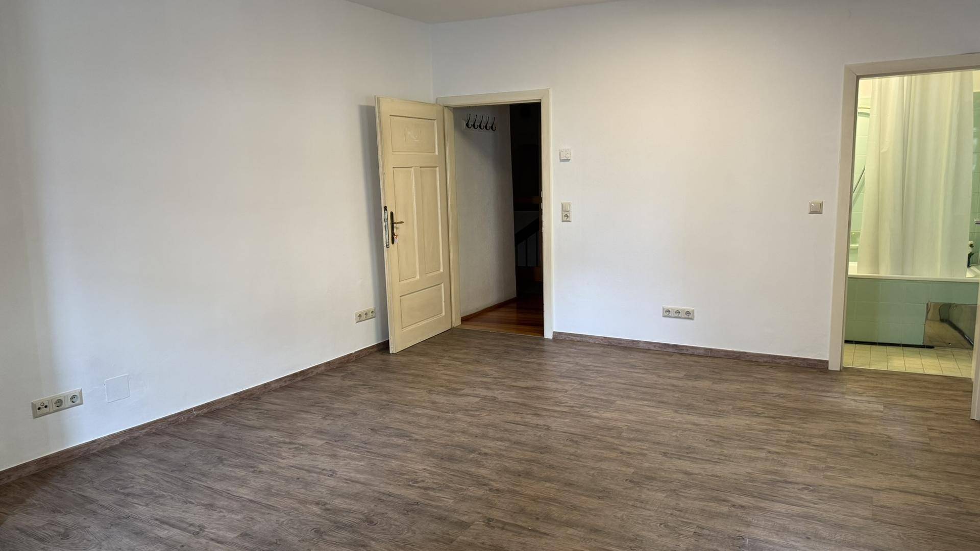 Ansicht eines leeren Zimmers mit Laminatboden und offener Tür zum angrenzenden Badezimmer.