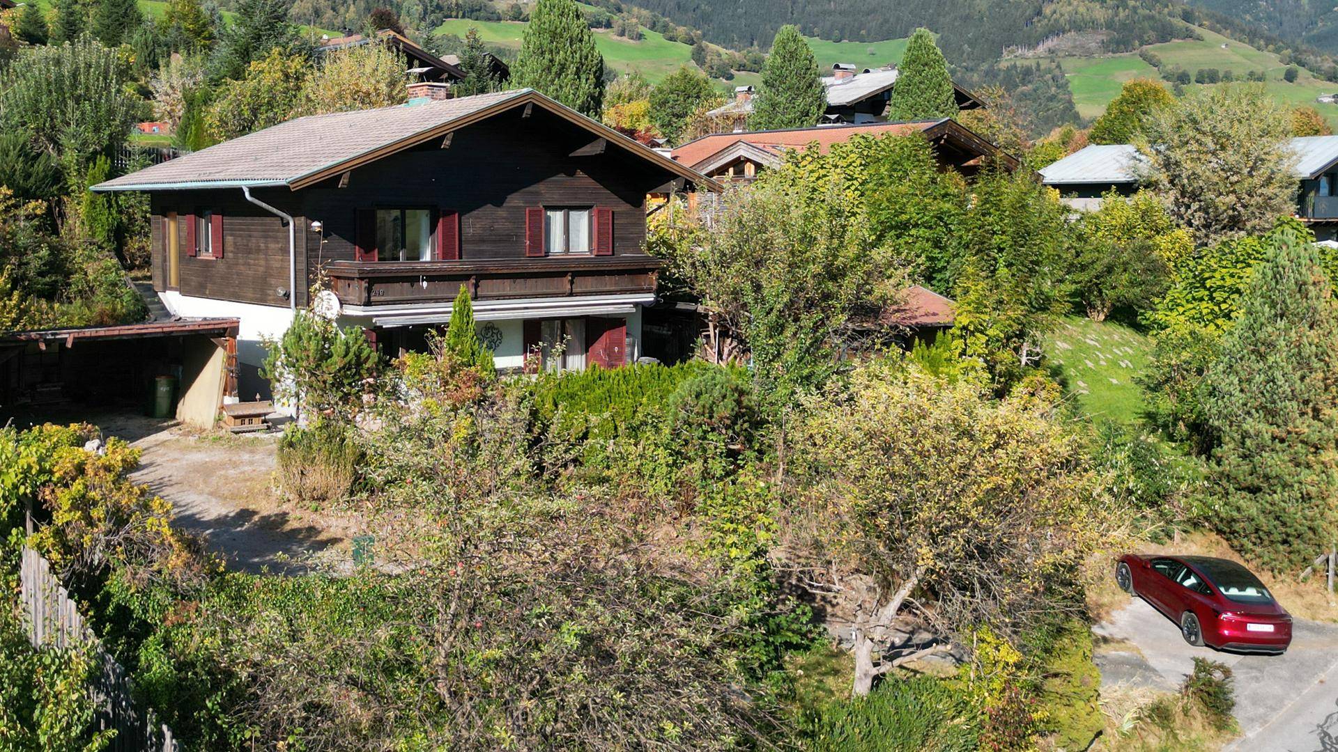 Idyllisches Holzhaus in den Bergen mit großem Grundstück, umgeben von viel Grün und weiteren Häusern.