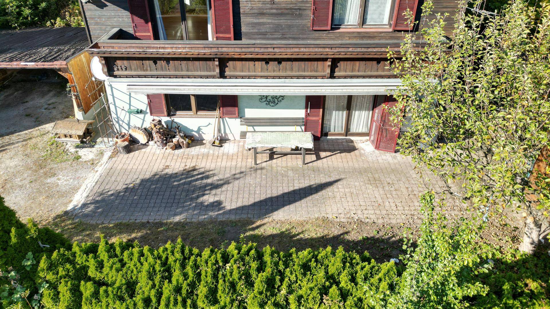 Gepflasterte Terrasse vor dem Haus mit Sitzgelegenheiten, umgeben von einer grünen Hecke.