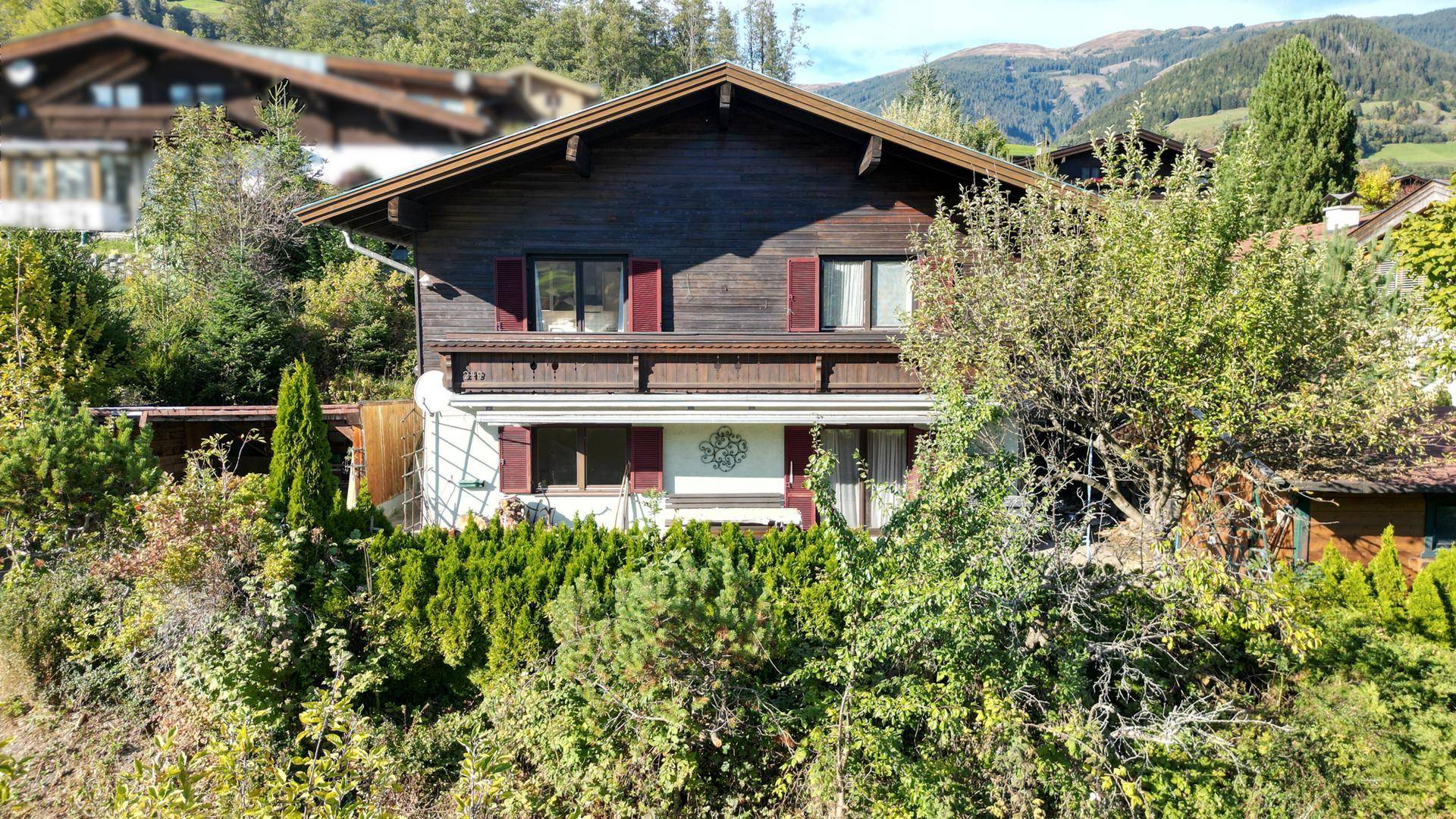 Charmantes Holzhaus in ländlicher Umgebung mit gepflegtem Garten und Bergblick im Hintergrund.