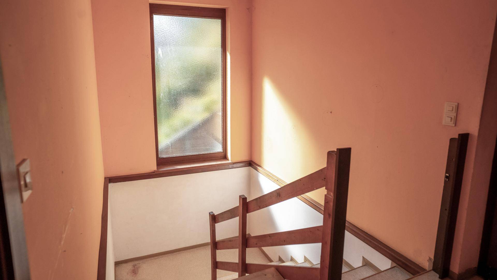 Treppenhaus mit Holzgeländer und Fenster, das natürliches Licht hereinlässt.