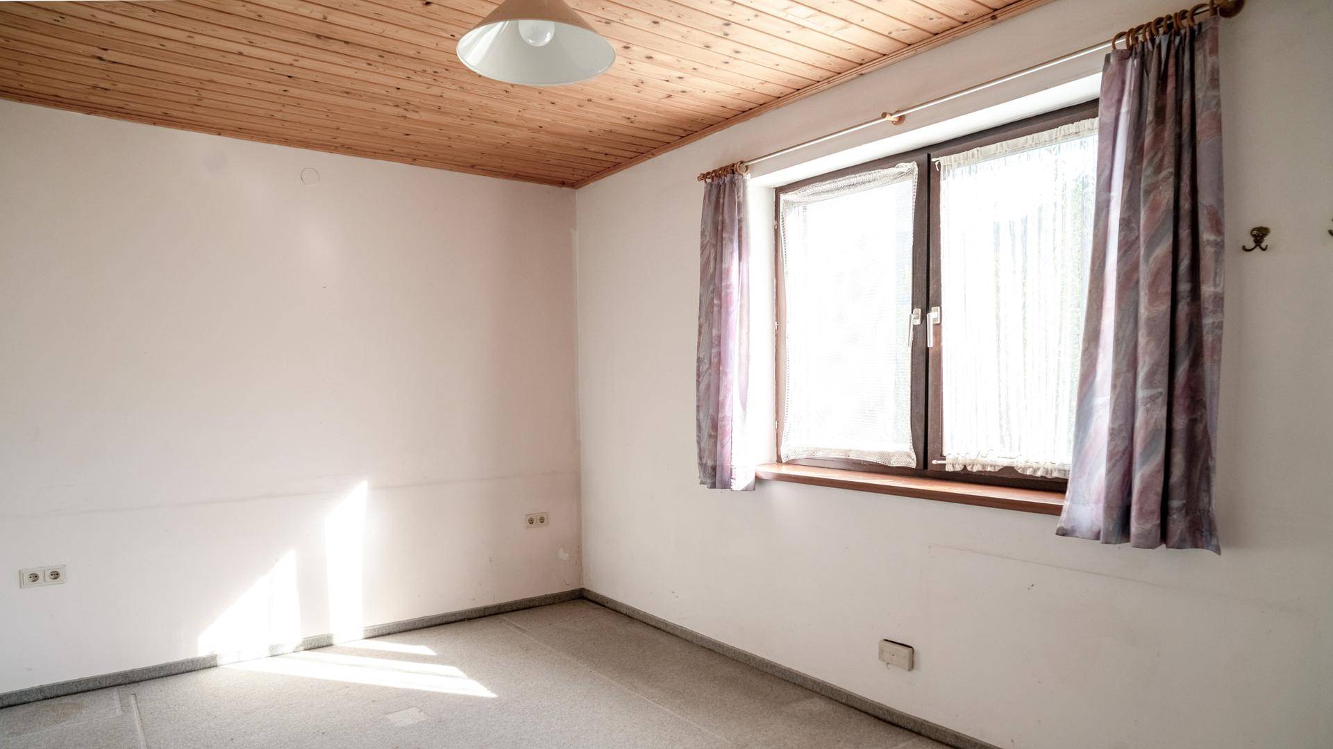 Helles Schlafzimmer mit Holzbalkendecke, Laminatboden und großem Fenster.