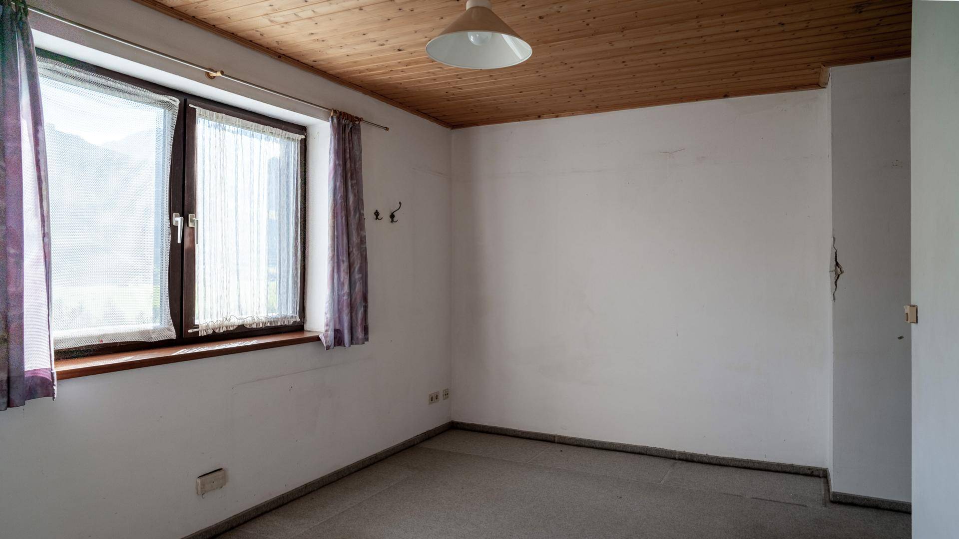 Schlafzimmer mit Holzbalkendecke, Laminatboden und Fenster, bereit zur individuellen Gestaltung.