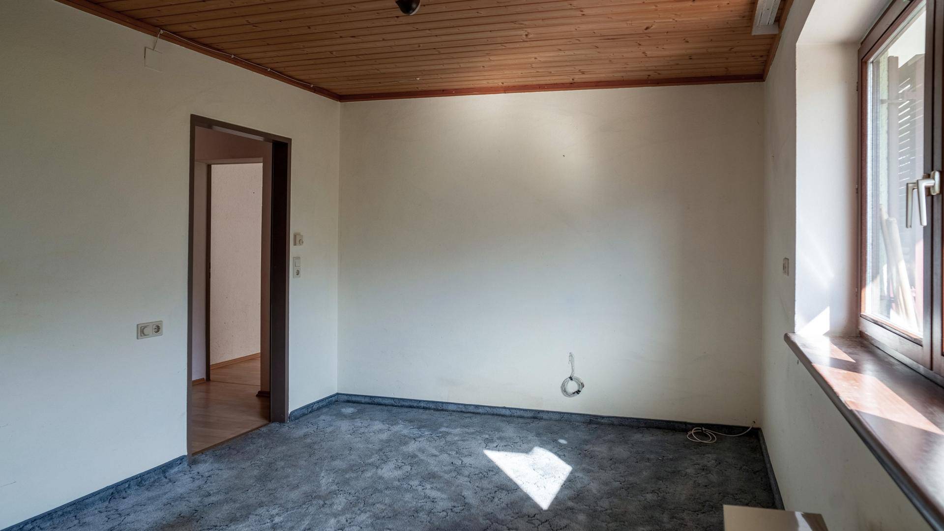 Schlafzimmer mit Holzbalkendecke, Laminatboden und Fenster, bereit zur Einrichtung.