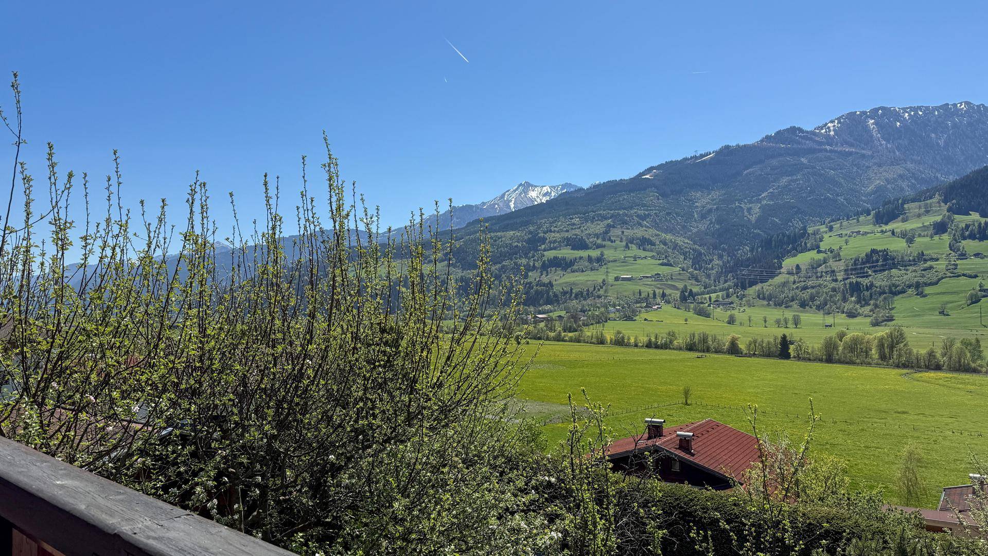 Malerischer Blick von einem Balkon über eine weite grüne Landschaft mit Bergen im Hintergrund.