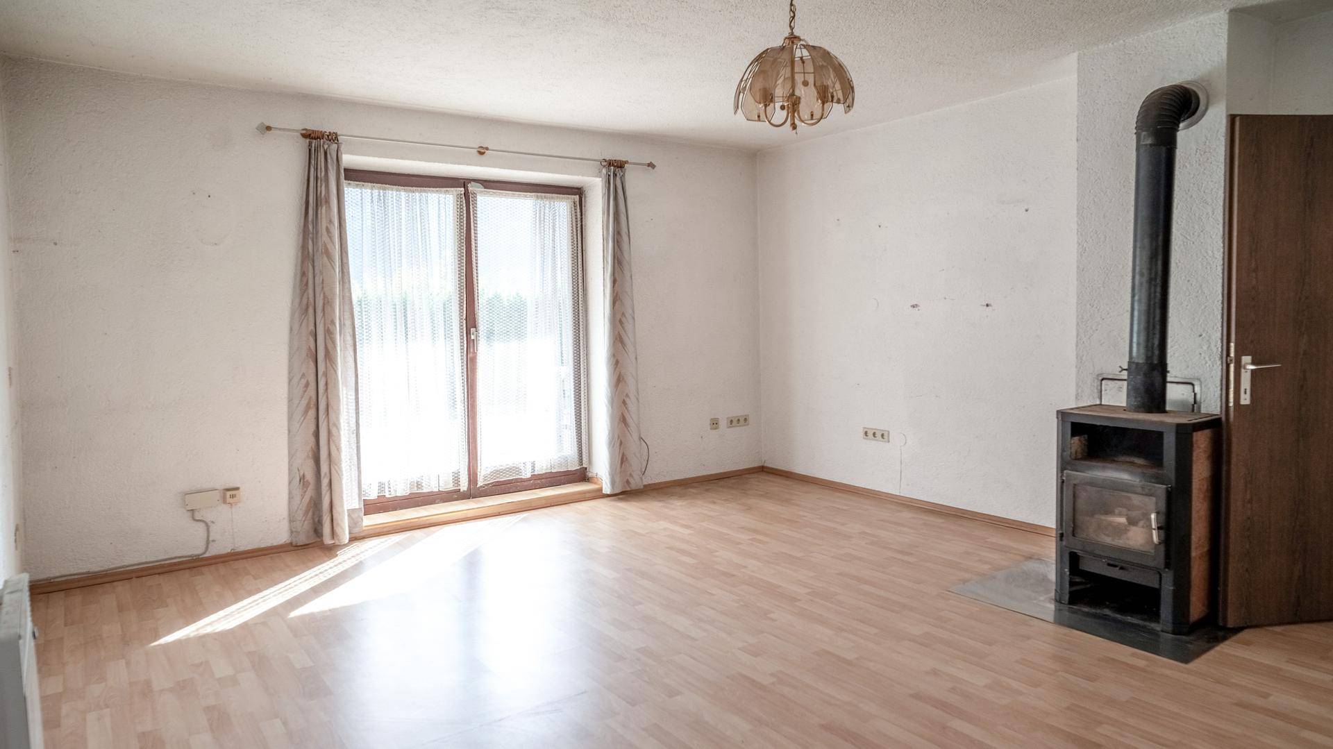 Helles Wohnzimmer mit Holzboden, Kaminofen und Zugang zu einem Balkon.