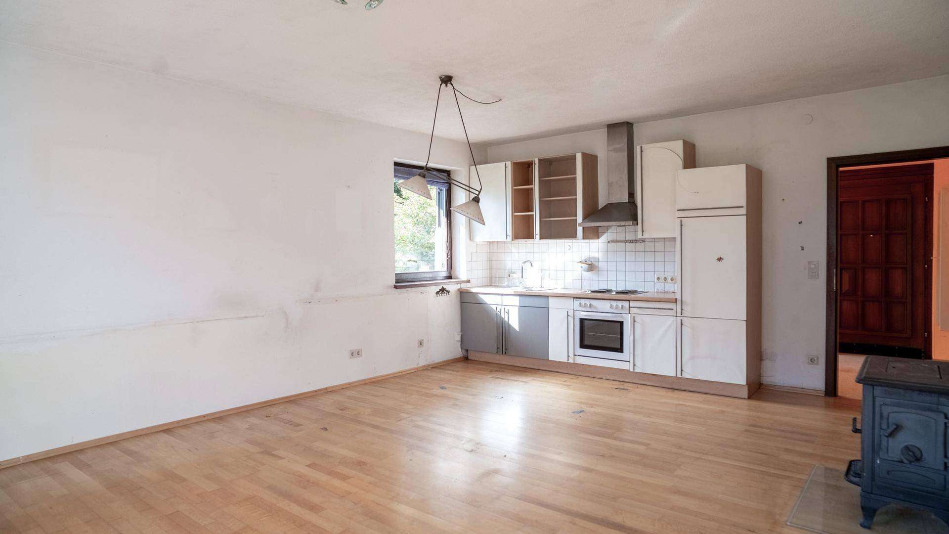 Offener Küchenbereich mit einfacher Einbauküche, Fenster und Holzboden.