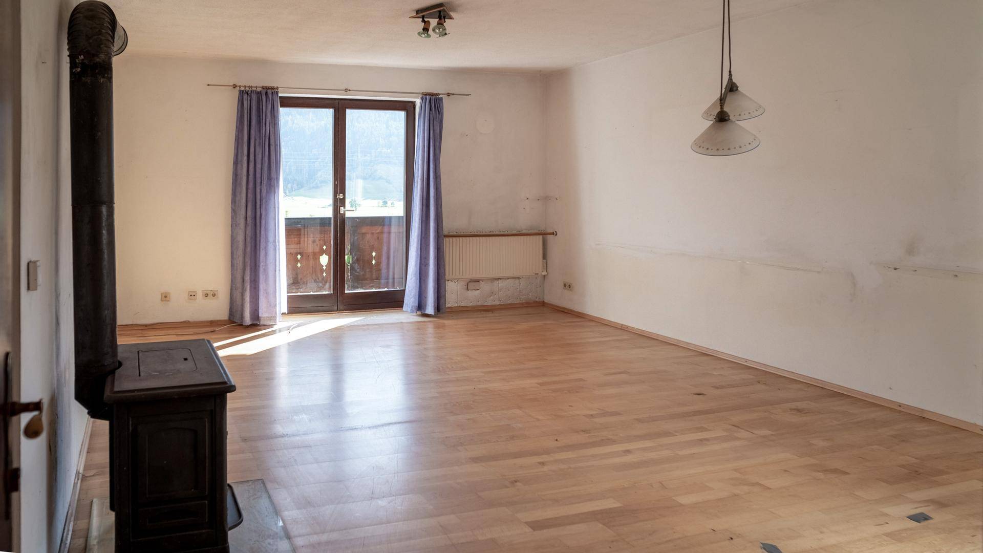 Geräumiges Wohnzimmer mit Kaminofen, Holzboden und Zugang zu einem Balkon.
