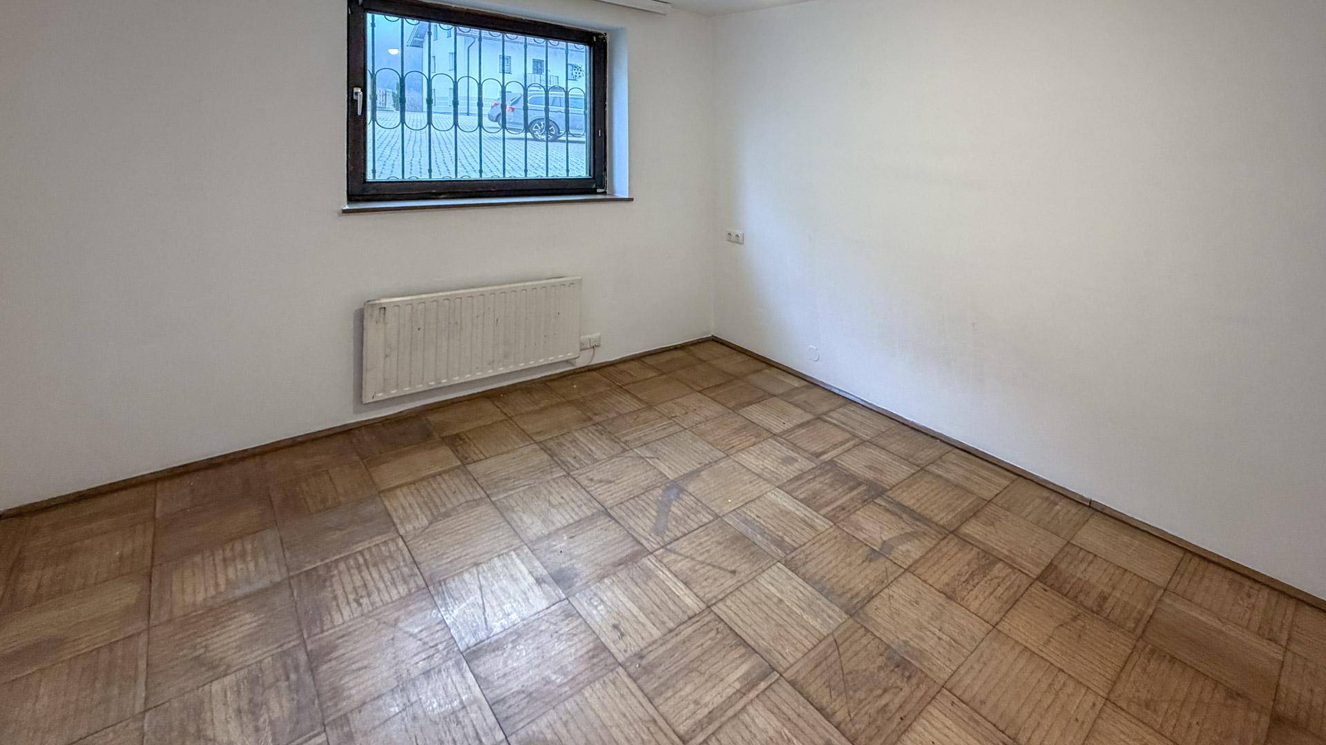 Leeres Zimmer mit Parkettboden, weißen Wänden und Fenster, ideal als Schlafzimmer.