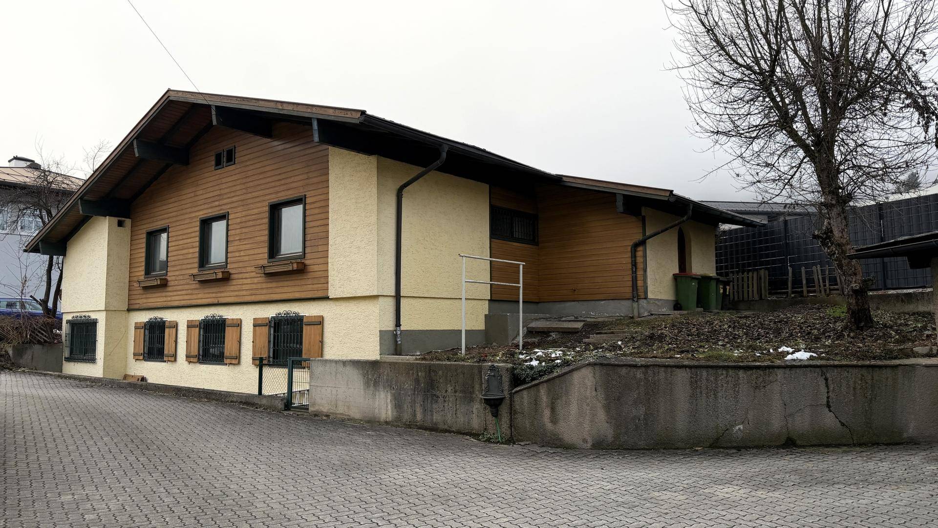 Rückansicht des Hauses mit Holzverkleidung und gepflastertem Zugangsbereich.