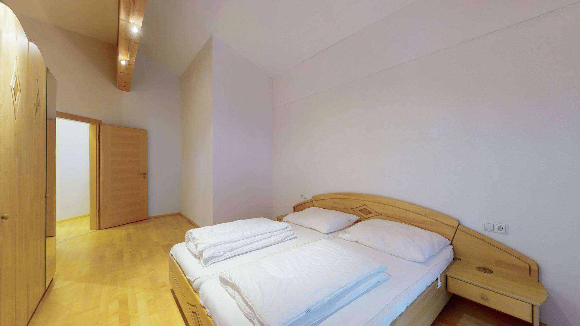 Schlafzimmer mit Doppelbett, Holzschrank und rustikalen Holzbalken an der Decke.