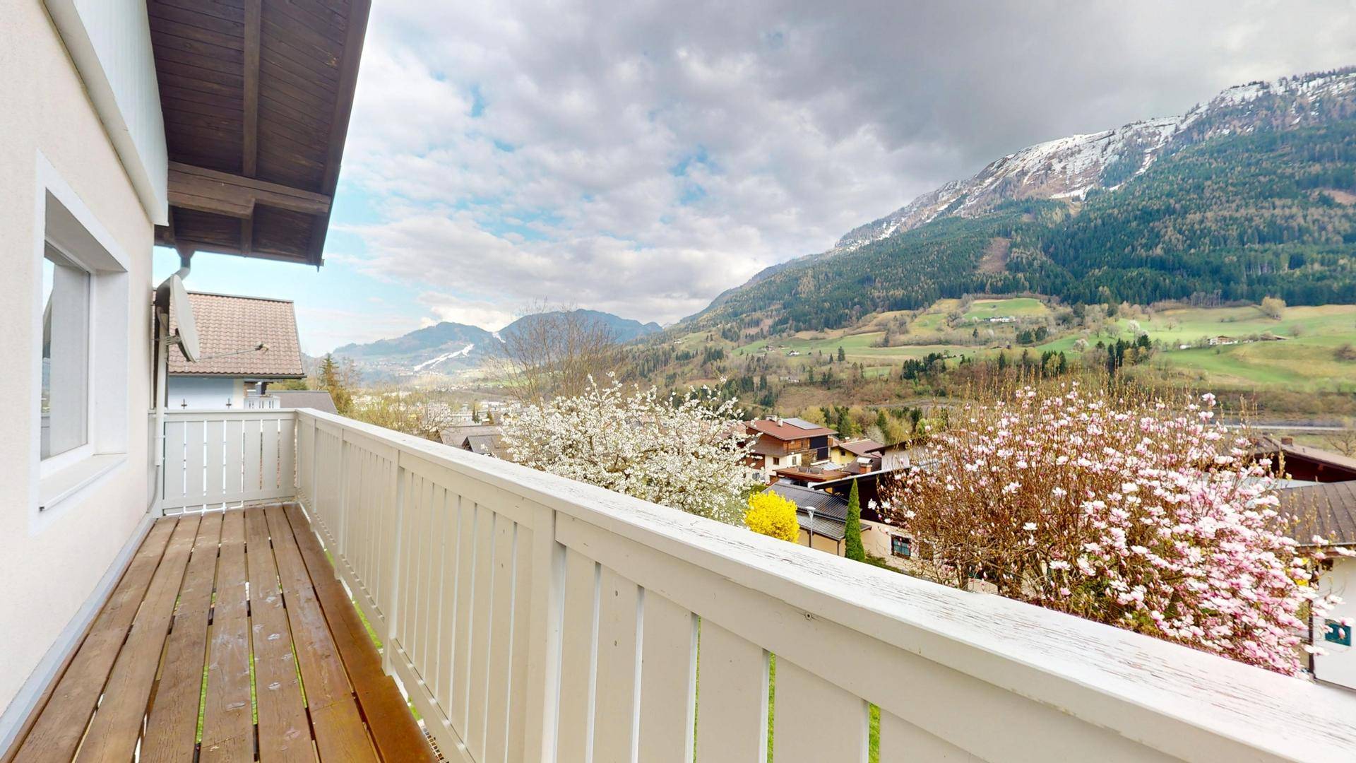 Langer Balkon mit Holzboden und Geländer, bietet weite Aussicht auf die Berglandschaft.