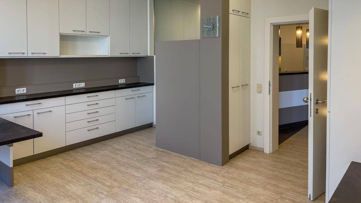 Geräumige Küche mit weißen Einbauschränken, dunkler Arbeitsplatte und hellem Vinylboden in Holzoptik.