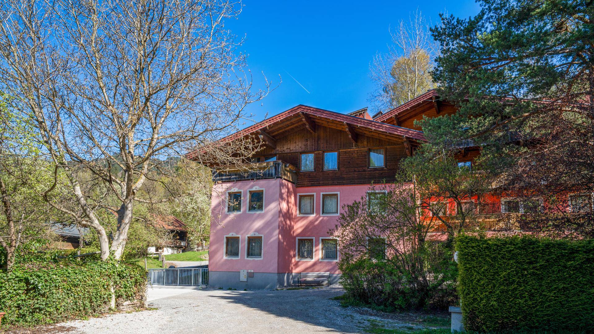Traditionelles Gebäude mit rosa Fassade und Holzelementen, eingebettet in eine grüne Landschaft.