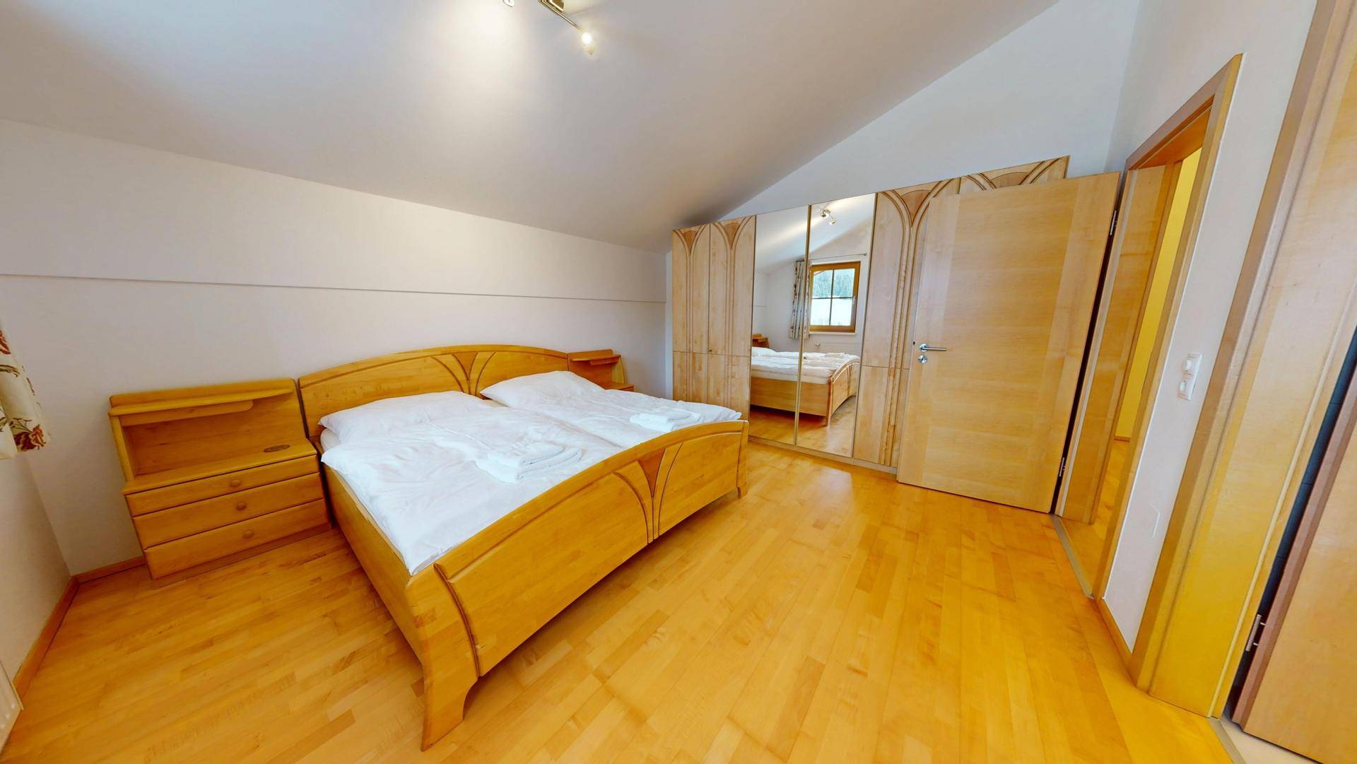 Gemütliches Schlafzimmer mit Holzbett, Parkettboden und großem Spiegelschrank.