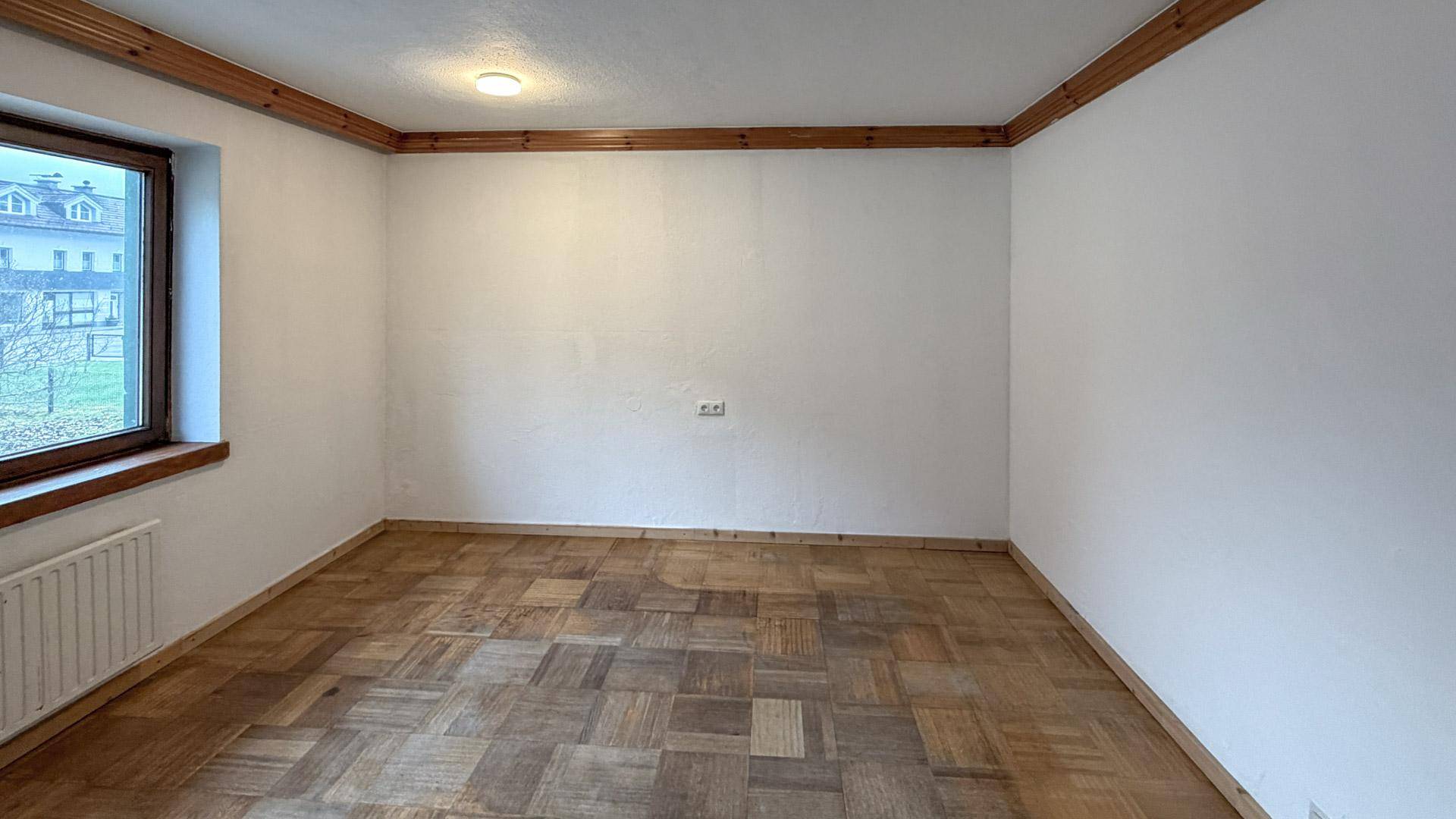 Leerer Raum mit Parkettboden, Fenster und Holzleisten an der Decke, bereit zur Neugestaltung.