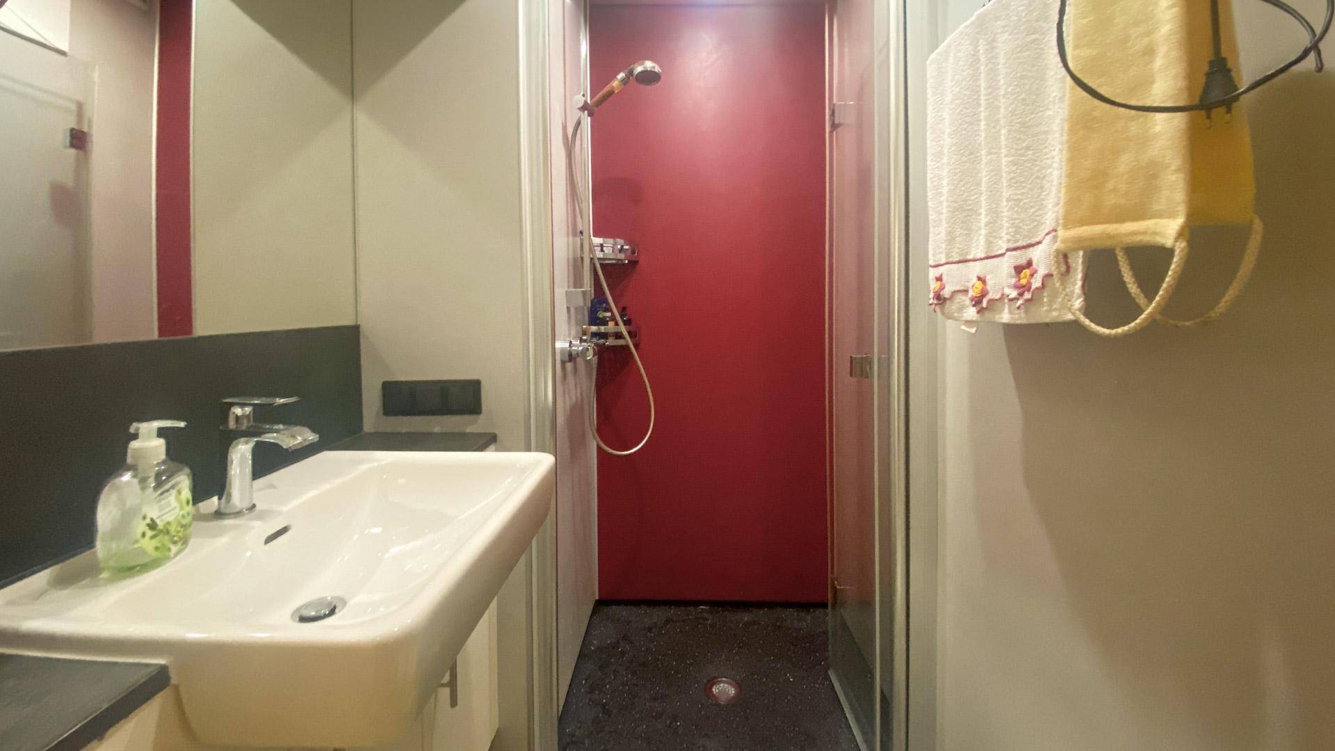 Modernes Badezimmer mit Dusche, Waschbecken und roter Akzentwand.