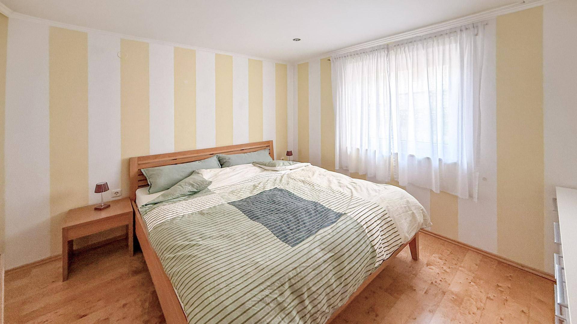 Helles Schlafzimmer mit Doppelbett, Holzboden und großen Fenstern für viel Tageslicht.