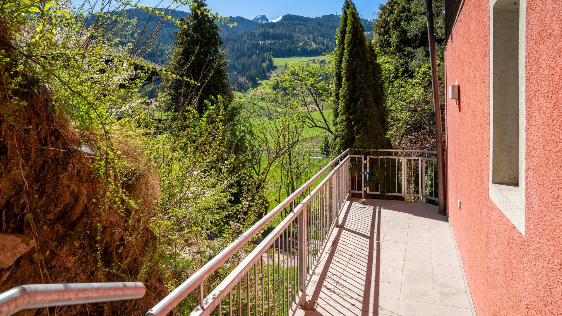 Sonniger Balkon mit Metallgeländer und weitem Blick auf die grüne Landschaft.