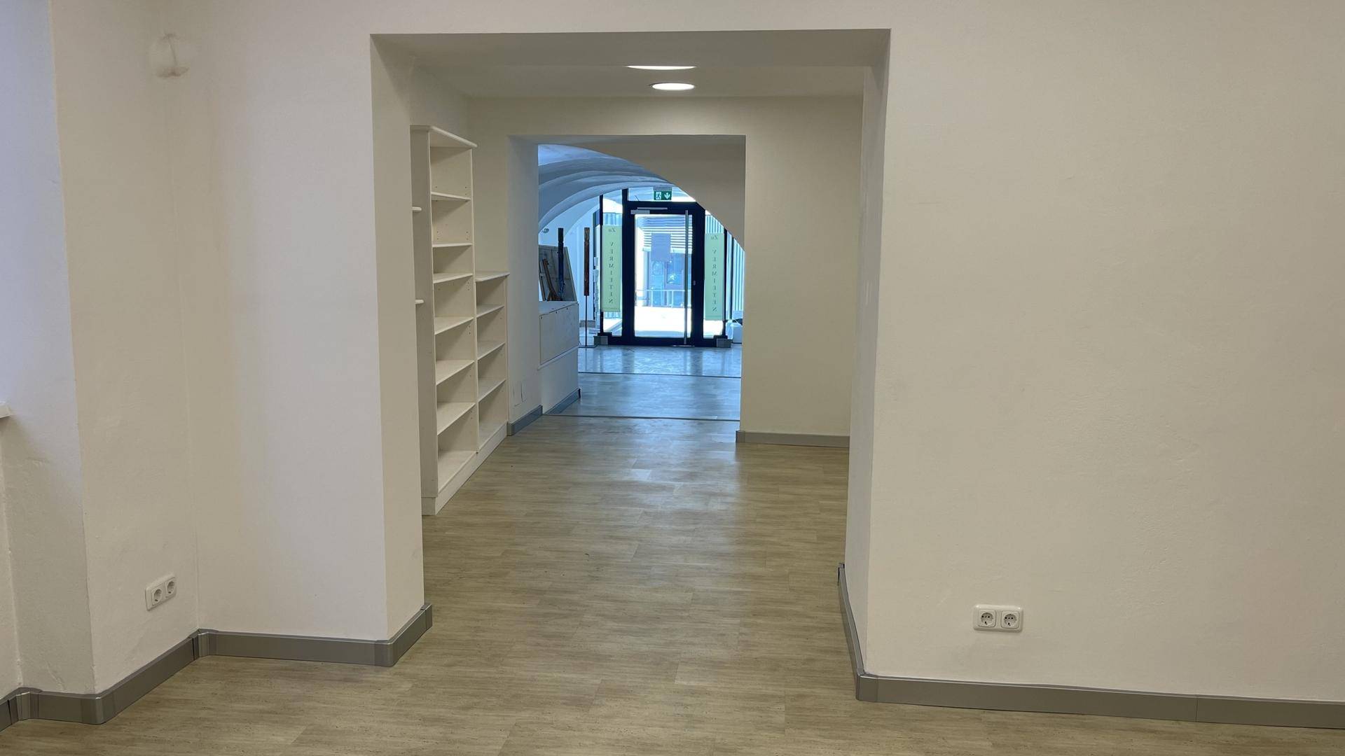 Heller Flur mit Holzoptikboden und Einbauregalen, der zu einem weiteren Bereich führt.