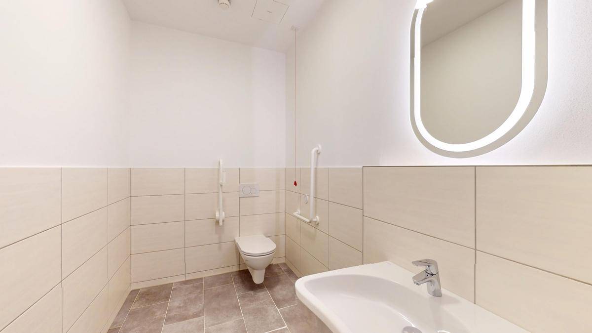 Barrierefreies Badezimmer mit Haltegriffen, wandhängender Toilette und modernem Waschbecken.