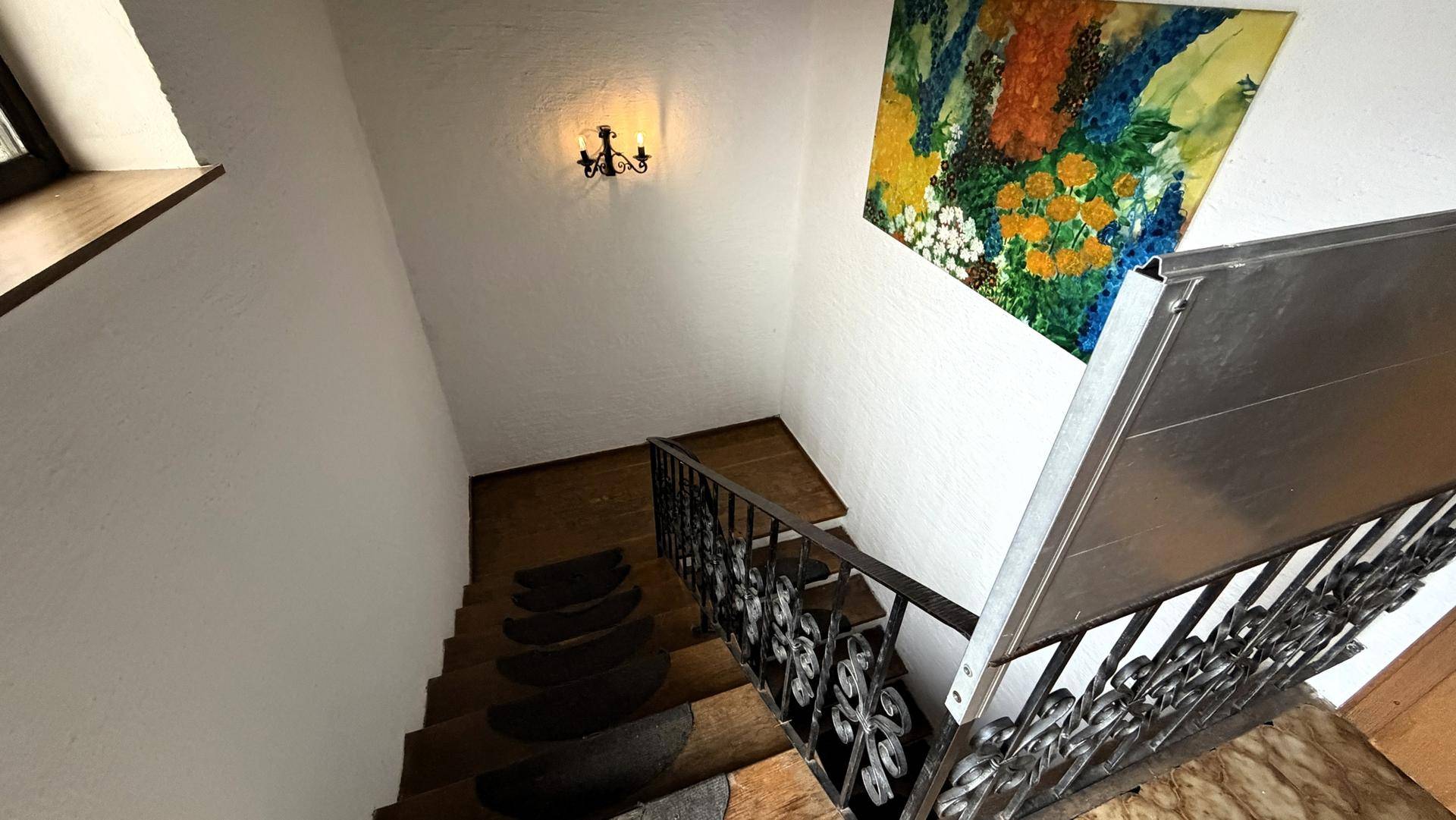 Treppenhaus mit schmiedeeisernem Geländer und farbenfrohem Wandbild.