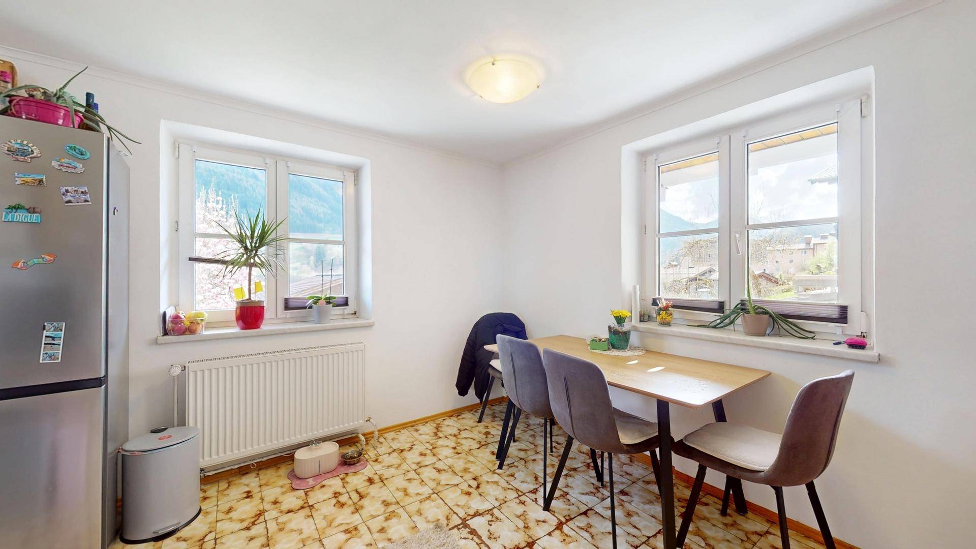 Heller Essbereich mit Esstisch, Stühlen und großem Kühlschrank, mit Blick auf die Berge.