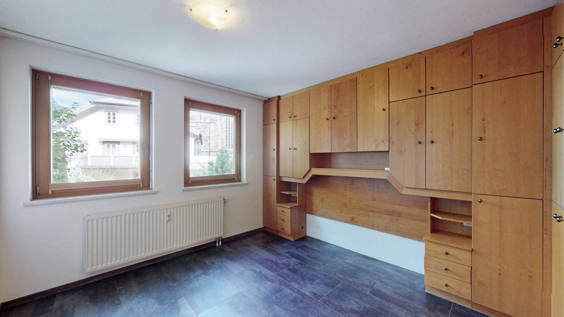 Schlafzimmer mit umfangreichen Einbauschränken aus Holz und dunklem Fliesenboden.