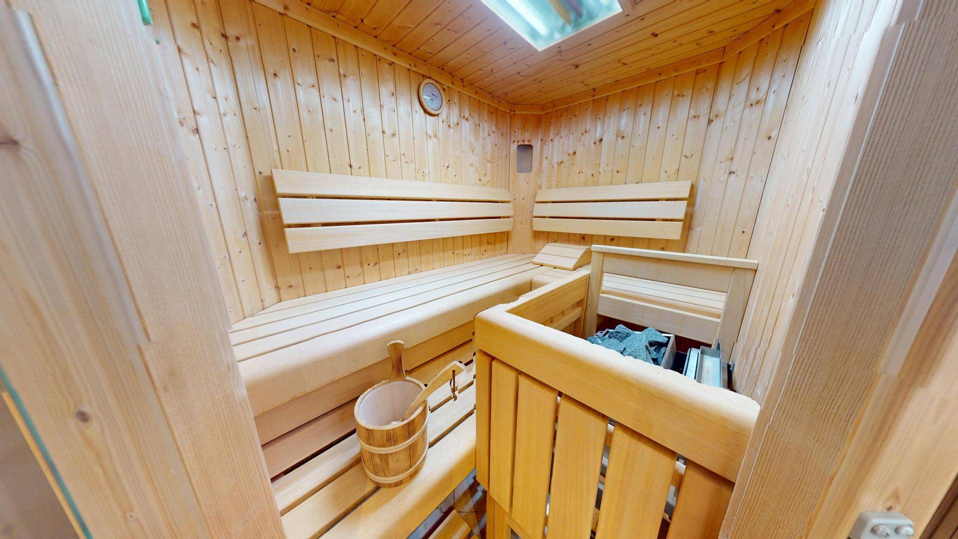 Innenansicht der holzvertäfelten Sauna mit Bänken und traditionellem Saunaofen.