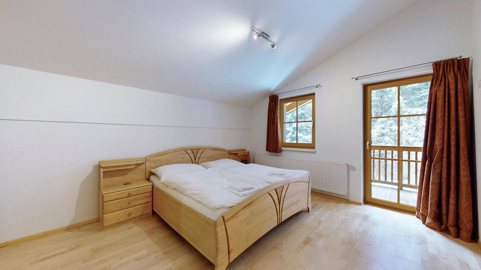 Helles Schlafzimmer mit Doppelbett, Holzmöbeln und Zugang zu einem kleinen Balkon.
