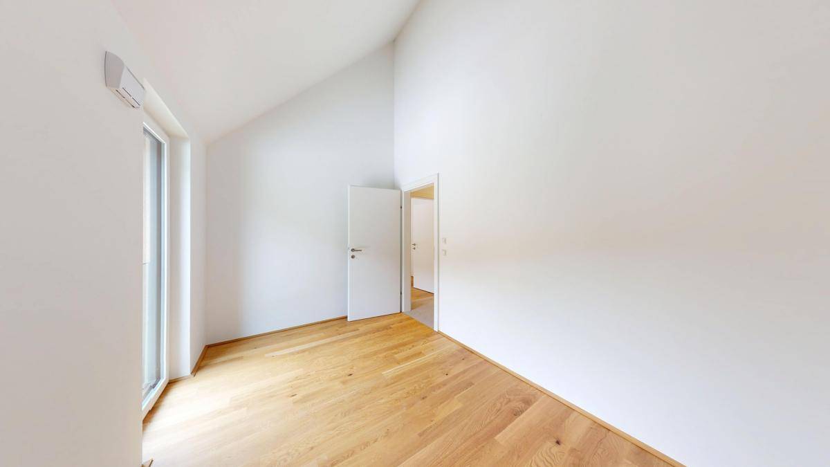 Helles Schlafzimmer mit Holzboden und einer Tür, die zu einem anderen Raum führt.