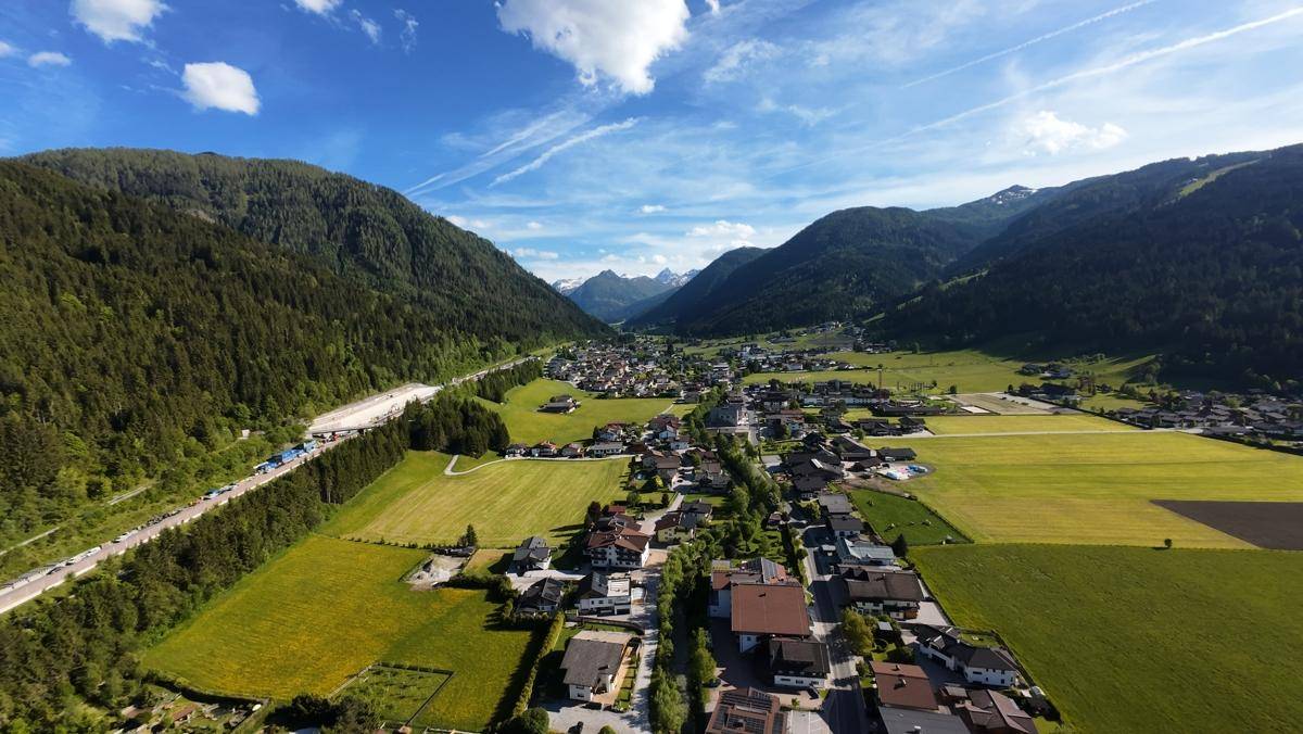 Panoramablick auf ein malerisches Tal mit einer Siedlung, umgeben von dichten Wäldern und hohen Bergen.