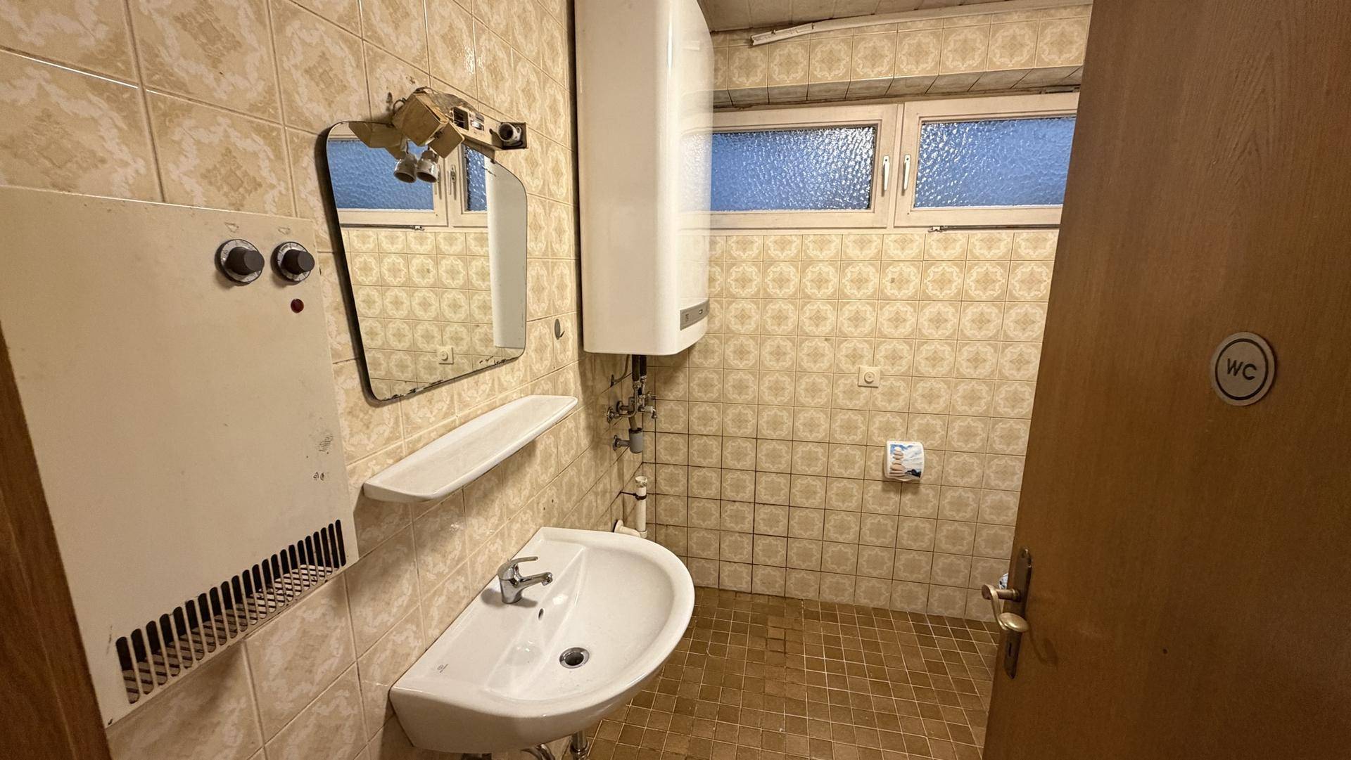 Kleines WC mit Waschbecken, Boiler und gemusterten Fliesen im Retro-Stil.