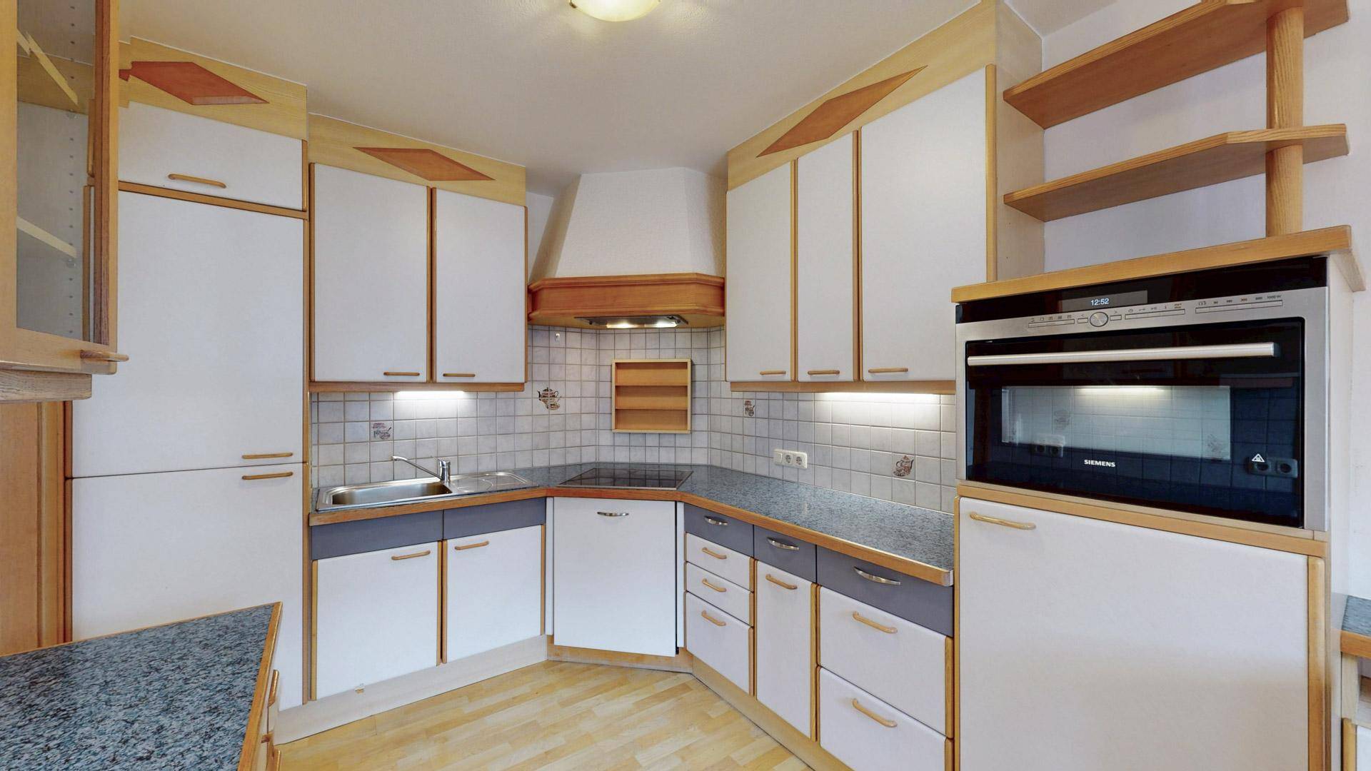Funktionale Küche mit weißen und holzfarbenen Schränken, integrierten Geräten und Fliesenboden.