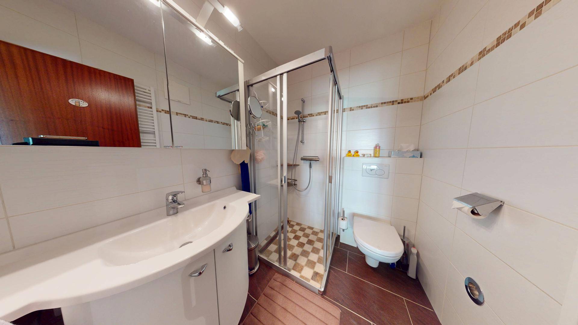 Badezimmer mit Duschkabine, Waschbecken und wandhängendem WC, gefliest in Weiß und Braun.