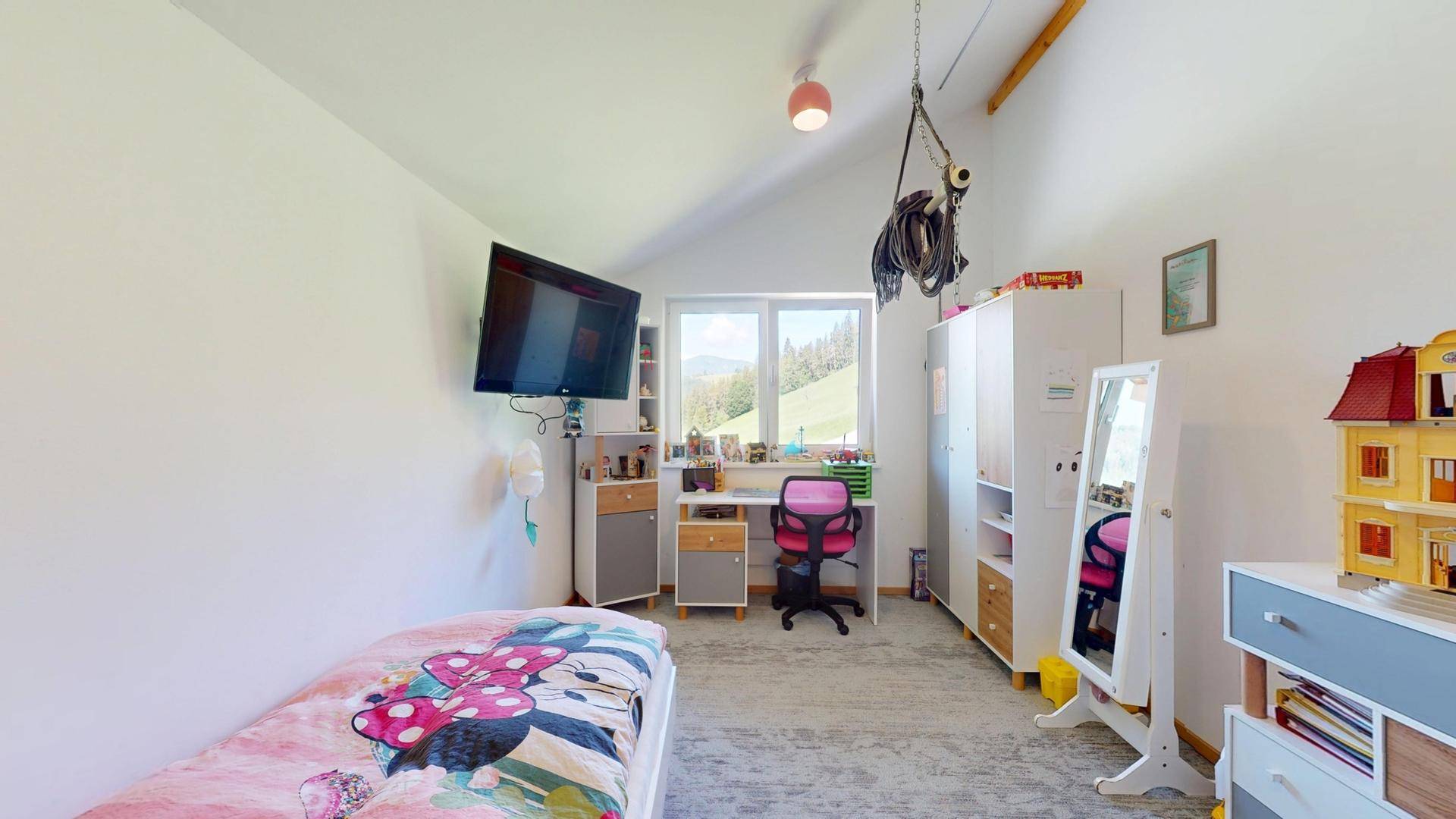 Freundliches Kinderzimmer mit Bett, Schreibtisch und Blick auf die grüne Landschaft.