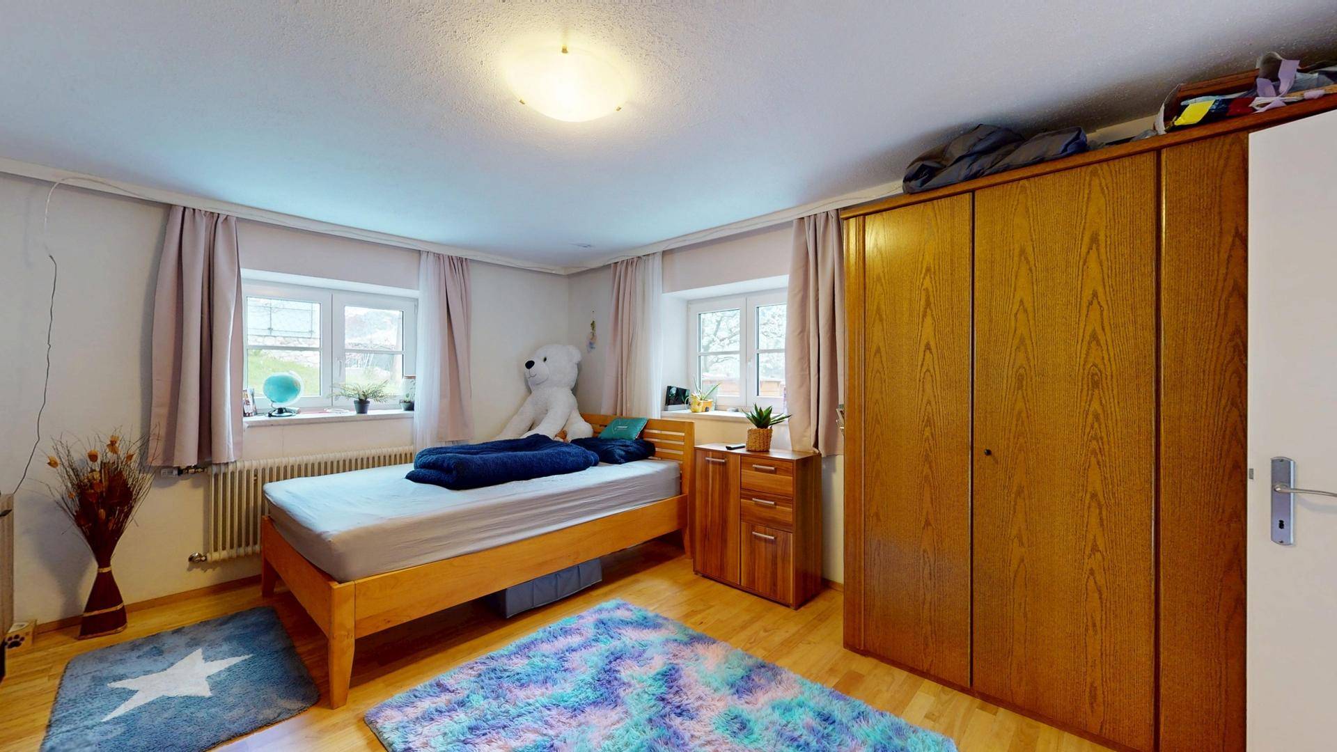 Gemütliches Kinderzimmer mit Einzelbett, Holzschrank und bunten Teppichen.