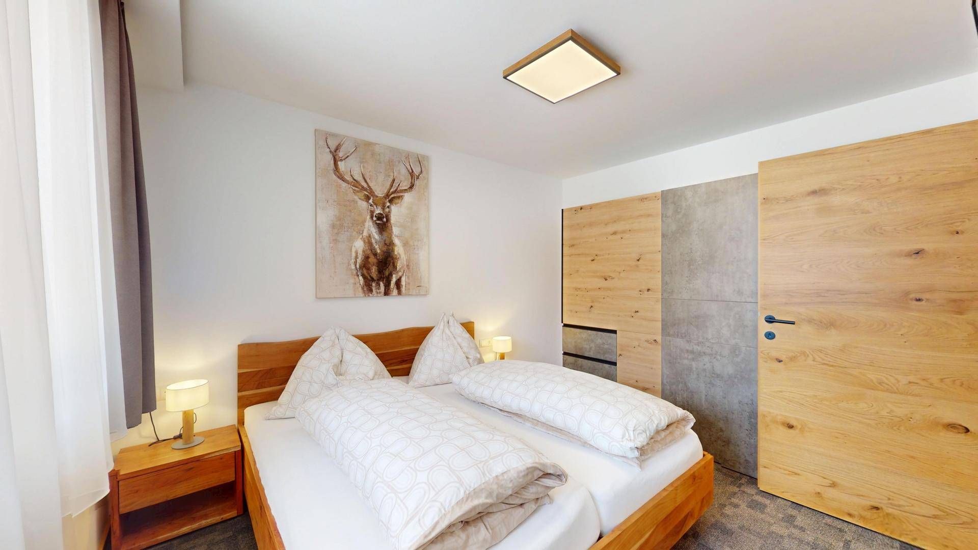 Helles Schlafzimmer mit Doppelbett, Holzschrank und Hirschbild.