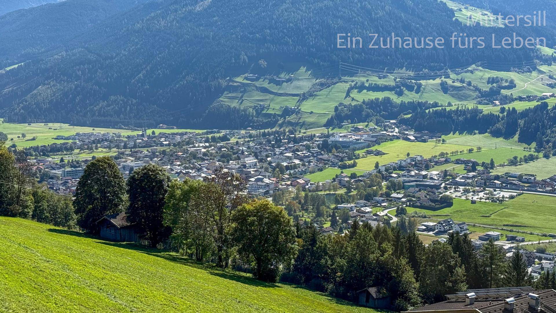 Weitläufige Landschaft mit grünen Hügeln und einem Dorf im Tal.
