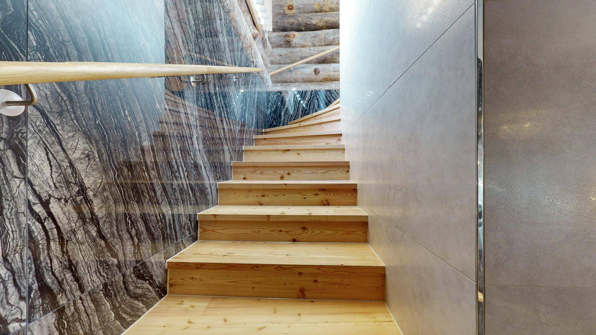 Elegante Holztreppe mit modernem Geländer und Marmorwandverkleidung, die die Etagen verbindet.