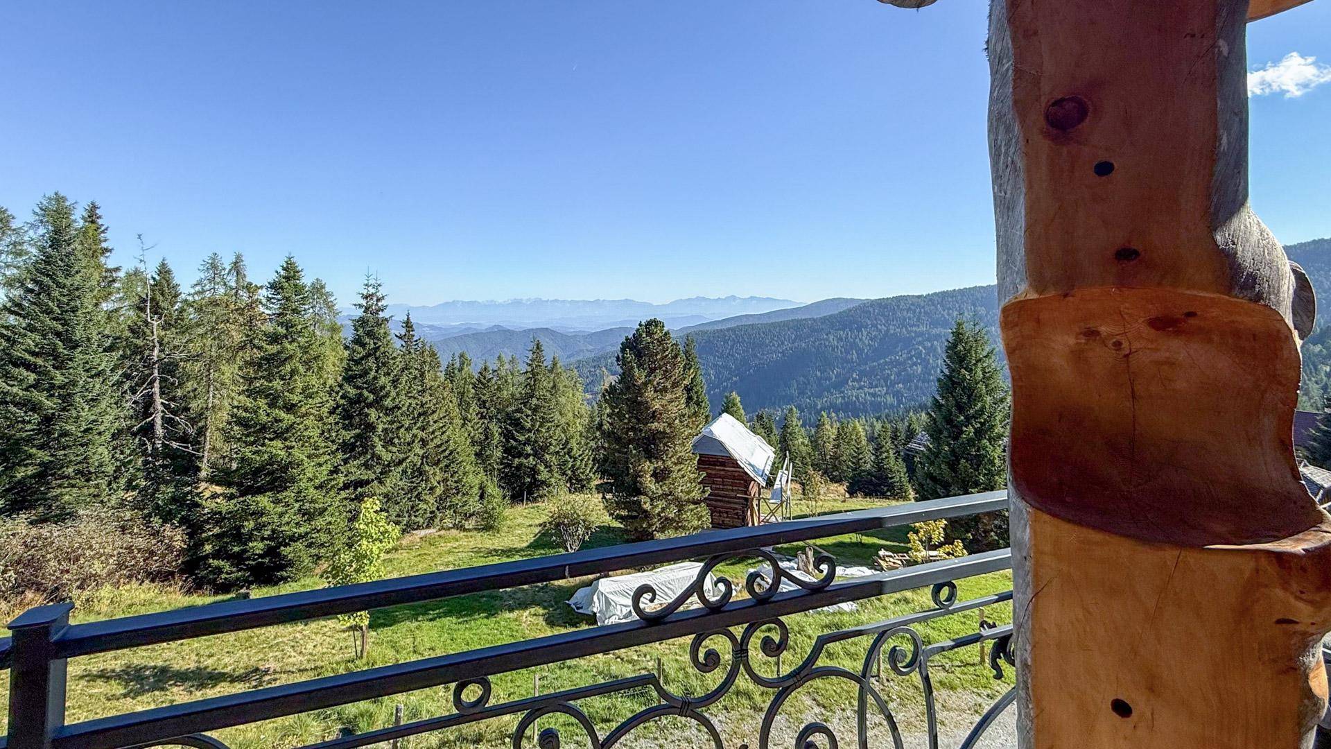 Weitläufiger Ausblick auf die alpine Landschaft mit Wäldern und Bergen von einem Balkon.
