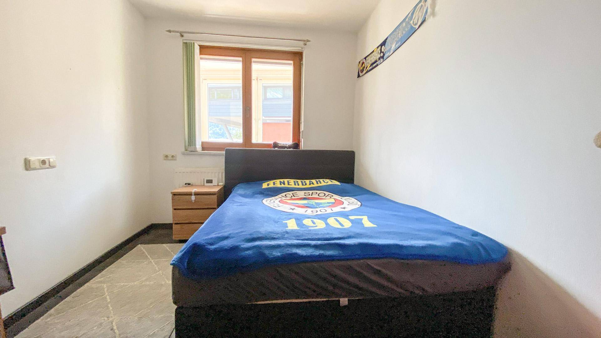Schlafzimmer mit Einzelbett, Nachttisch und Fenster.