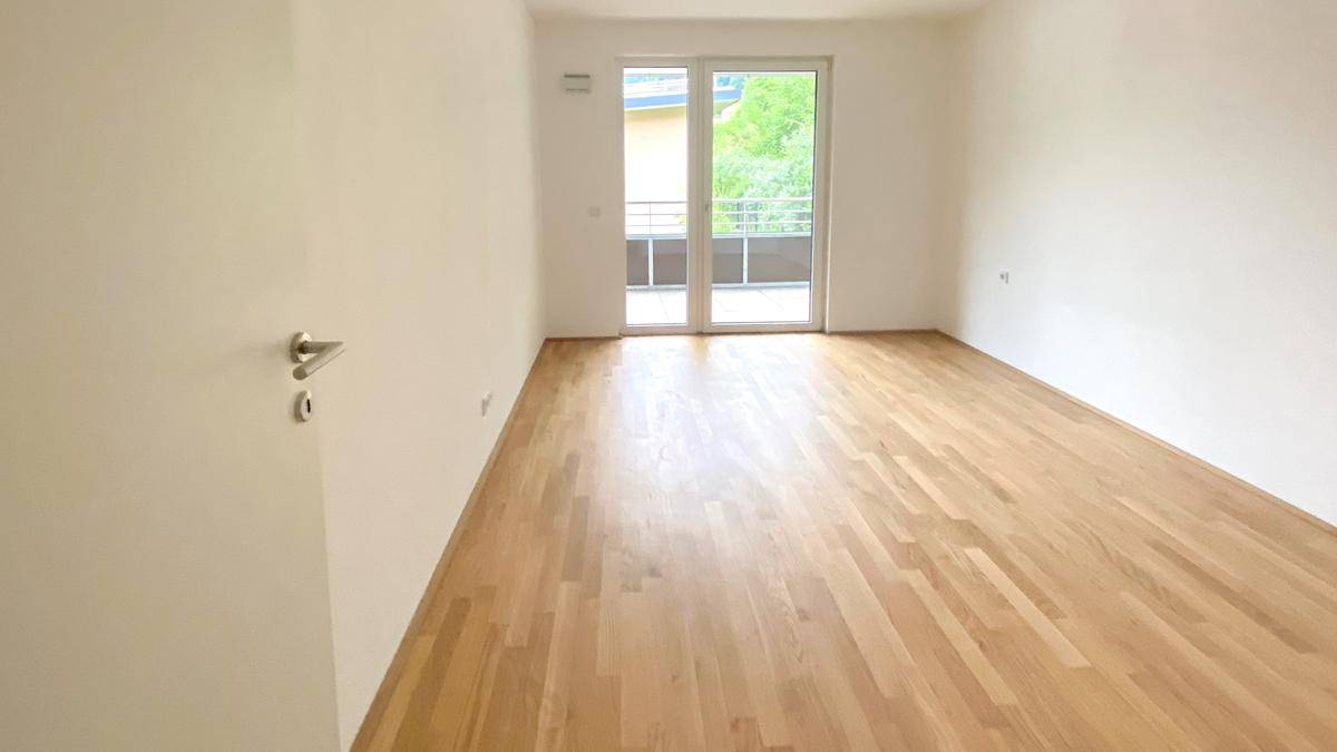 Heller Raum mit Parkettboden und großen Fenstern, die Zugang zum Außenbereich bieten.